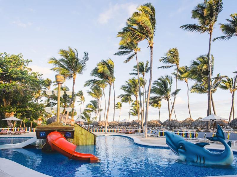 Área de piscina con toboganes de agua y palmeras en un resort tropical frente al mar.