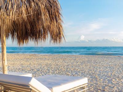 Zwei Liegestühle unter einem Strohdach am sandigen Strand mit Blick auf das Meer.