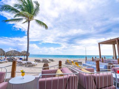Strandrestaurant mit Sitzgelegenheiten, Palmen und Blick auf den Ozean bei klarem Himmel.