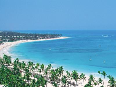 Lunga spiaggia di sabbia bianca con palme e acqua blu limpida sotto un cielo senza nuvole.