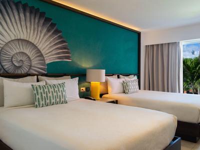 Camera d'hotel moderna con due letti, decorazione murale verde e balcone con vista sulle palme.