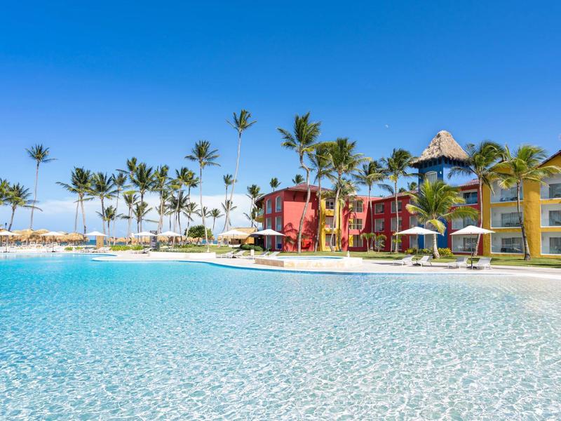 Acqua limpida di un resort con edifici colorati e palme sotto un cielo blu.