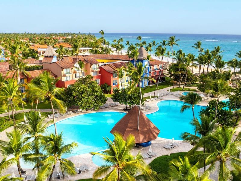 Vista di un resort tropicale con piscina, palme e oceano sullo sfondo con tempo soleggiato.