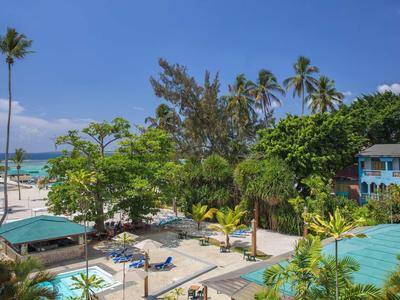 Tropischer Strand mit Palmen, blauer Lagune, Sonnenschirmen und kleinen blauen Hütten am Meer.
