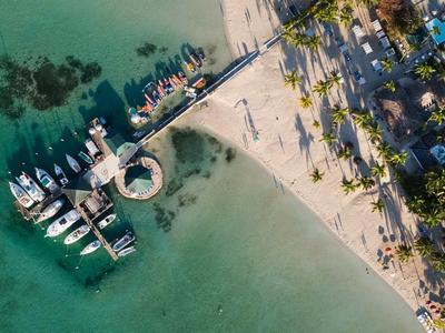 Widok z lotu ptaka na plażę z czystą wodą, łodziami i molo obok palm.