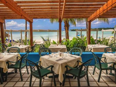 Open restaurant met tafelkleden en uitzicht op het strand en de zee onder een houten pergola.