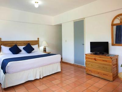 Lichte hotelkamer met tweepersoonsbed, houten meubels en tegelvloer.