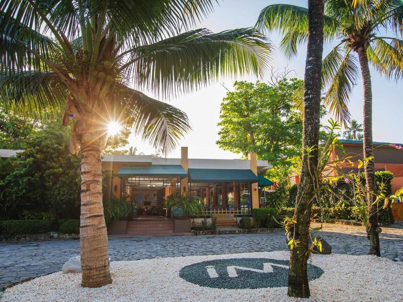 Hotel met tropische palmbomen en ochtendzonlicht in de tuin.