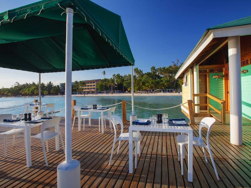 Terras met witte tafels en stoelen aan het water onder een heldere blauwe lucht.