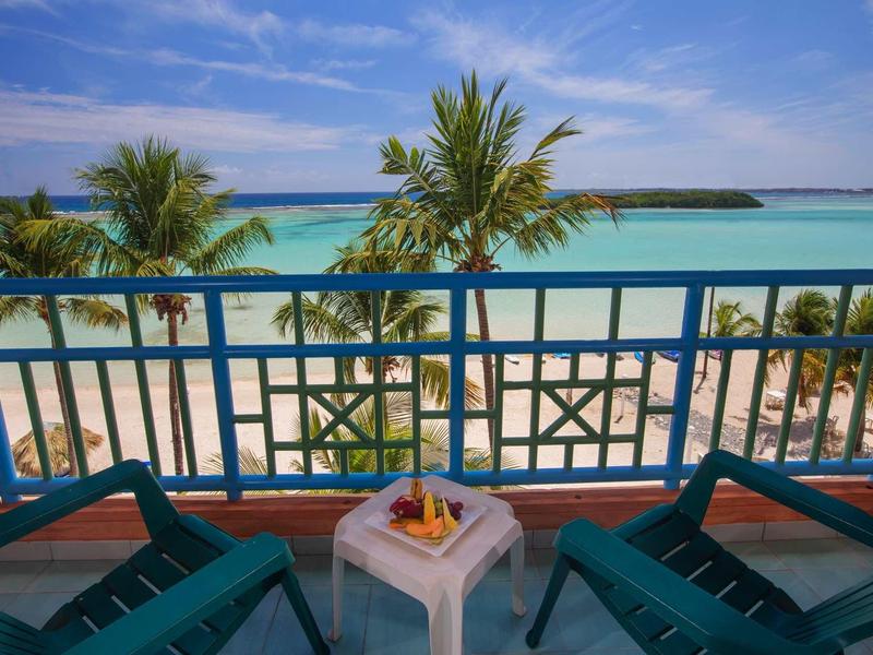 Uitzicht vanaf balkon met groene stoelen op tropisch strand en turquoise zee.