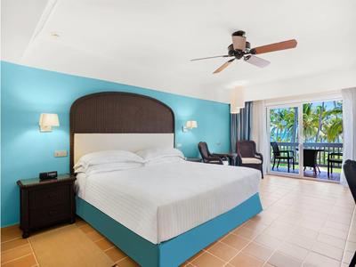 Moderní hotelový pokoj s velkou postelí, modrou zdí a balkonem s výhledem na moře.