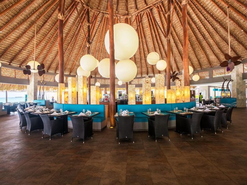 Velká kulatá restaurace s mnoha stoly pod doškovou střechou a kulatými světly