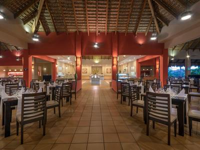 Groot open restaurant met houten tafels en stoelen onder een hoog rieten dak.