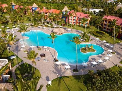 Hotelcomplex met groot zwembad omgeven door palmbomen en comfortabele ligstoelen in een tropische tuin.