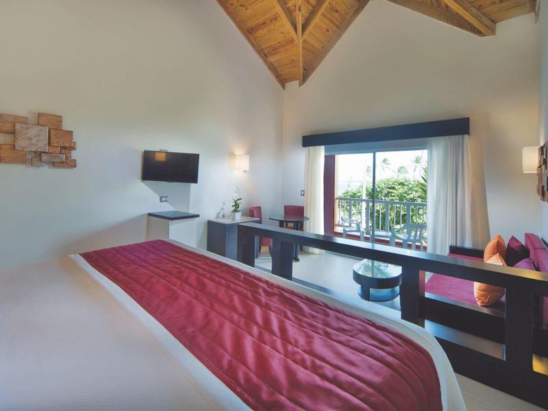 Moderne hotelkamer met zichtbare houten balkenplafond, groot bed en balkon met tuinzicht.