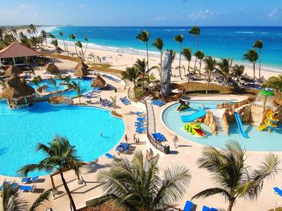 Large hotel resort with pools, water slides, and lounge chairs on a palm-lined beach.