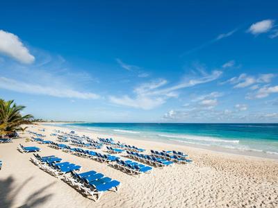 Beach with blue lounge chairs, white sand, and clear blue sky by the sea