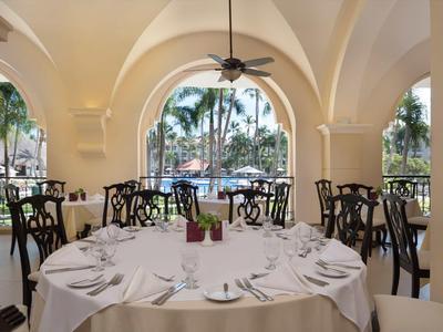 Elegant dining area with round tables and palm views through arched windows.