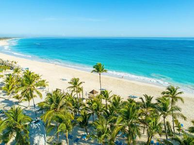 White sandy beach with palm trees and clear blue sea under bright blue sky.