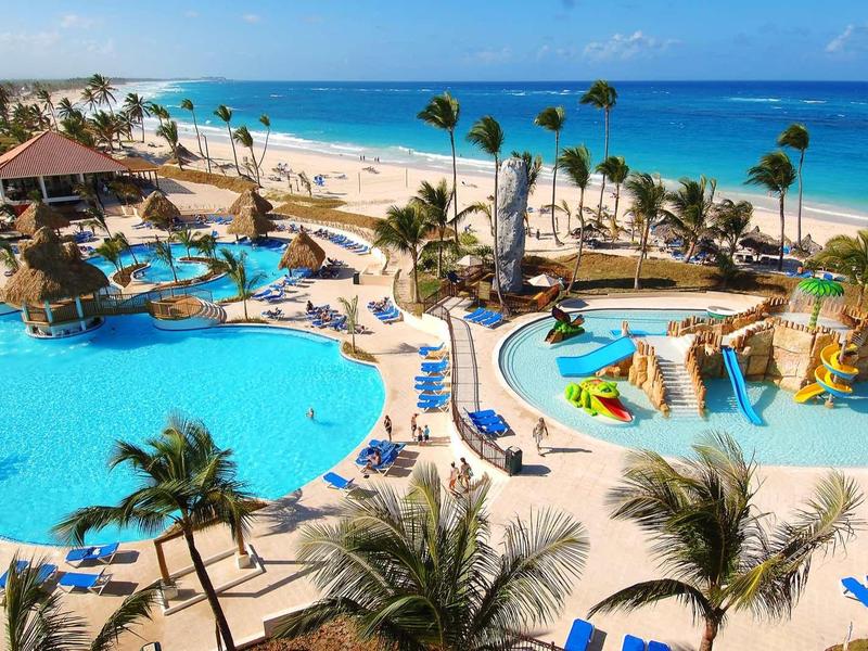 Large hotel resort with pools, water slides, and lounge chairs on a palm-lined beach.