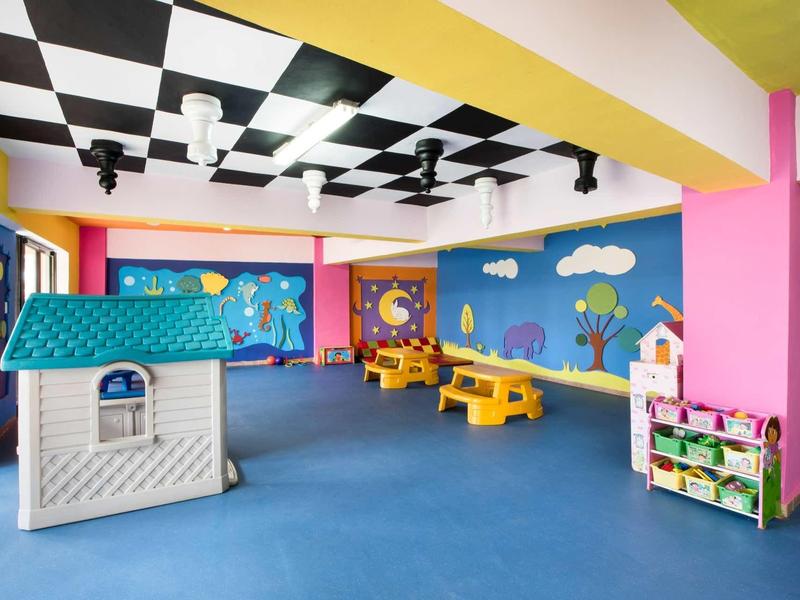 Colorful children's playroom with playhouse, wooden tables, and bright wall murals in a hotel