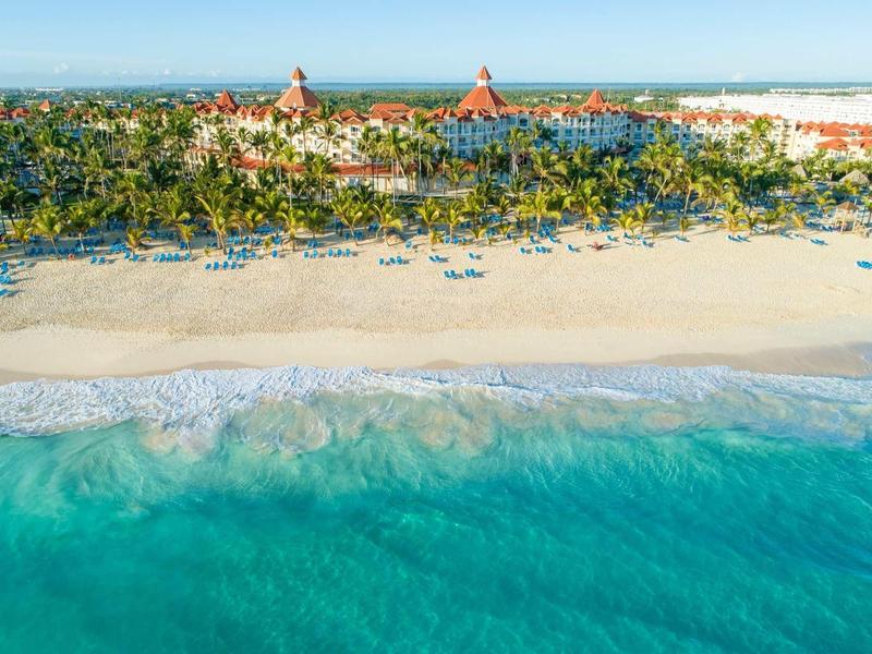 View of a large beachfront hotel with turquoise sea and sun umbrellas.