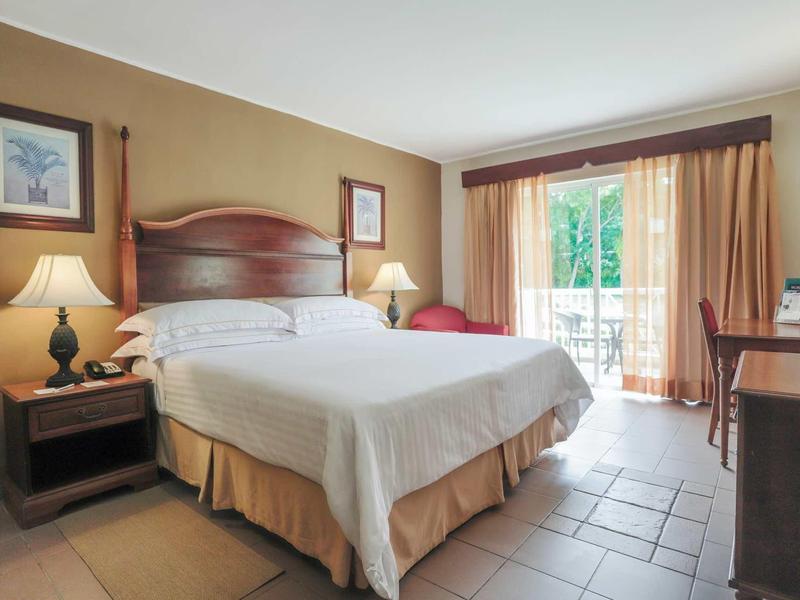 Bright hotel room with large bed, bedside lamps, and balcony with curtains.