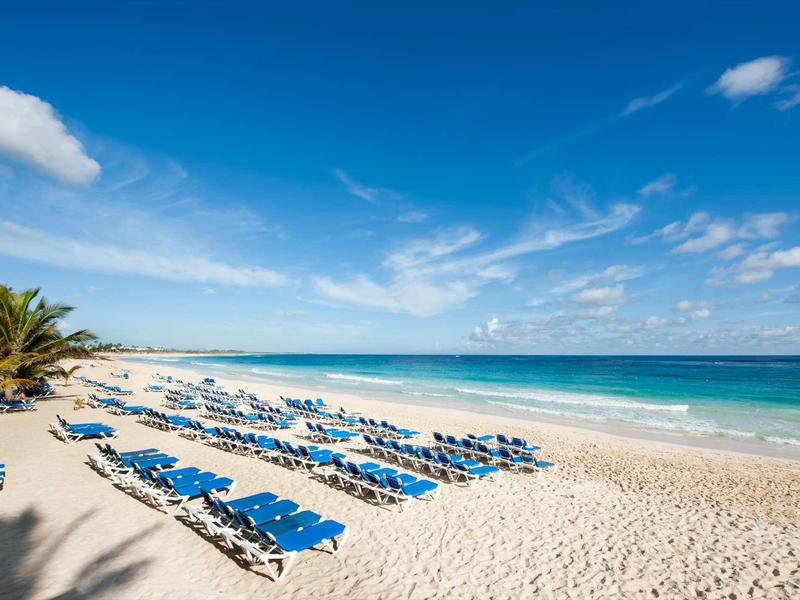 Beach with blue lounge chairs, white sand, and clear blue sky by the sea
