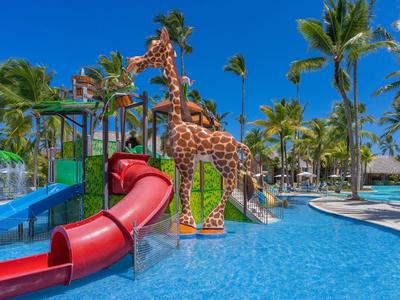 Kleurrijke kinderspeelplaats met glijbanen en giraffenfiguur in het zwembad van een tropisch resort.