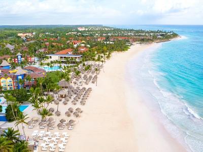 Lange witzandige strand met parasols, omgeven door tropische bomen en resorts.