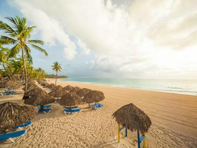 Leeg zandstrand met palmbomen en blauwe ligstoelen onder rieten daken bij zonsondergang.