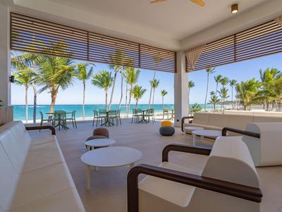 Offener Lounge-Bereich mit weißen Sitzmöbeln und Blick auf Palmen und Meer.