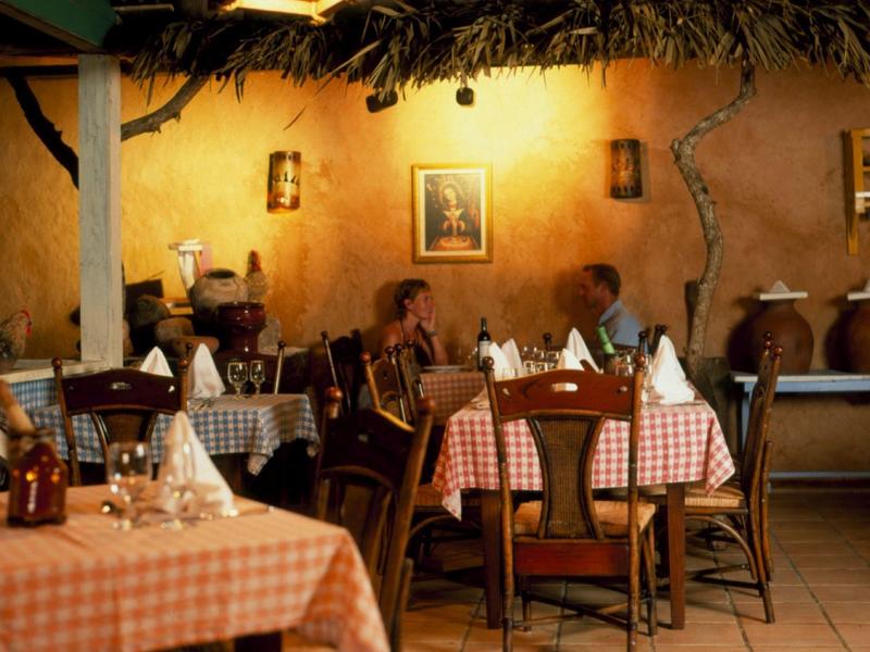 Knusse binnenrestaurant met geruite tafelkleden en warme verlichting, gasten aan het dineren.