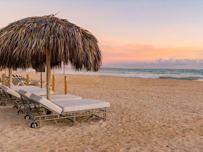 Lege ligstoelen onder strooien parasols op het strand bij zonsondergang.