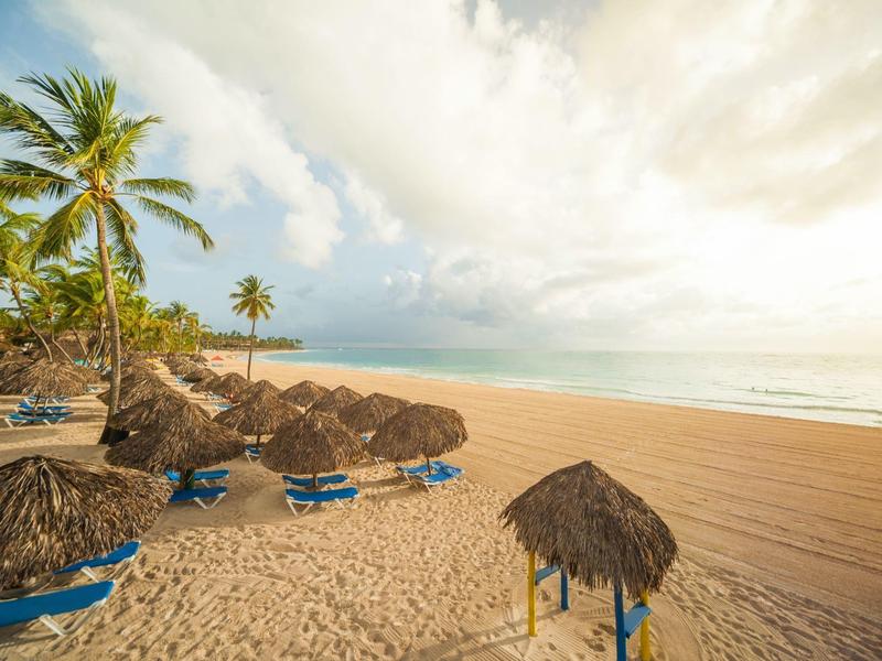 Leeg zandstrand met palmbomen en blauwe ligstoelen onder rieten daken bij zonsondergang.