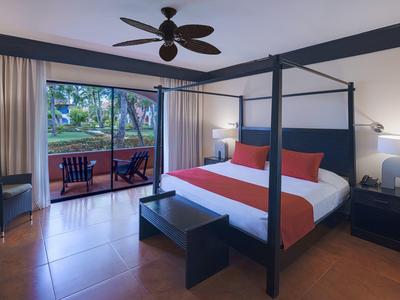 Chambre d'hôtel moderne avec lit à baldaquin, chaises sur la terrasse et vue sur le jardin.