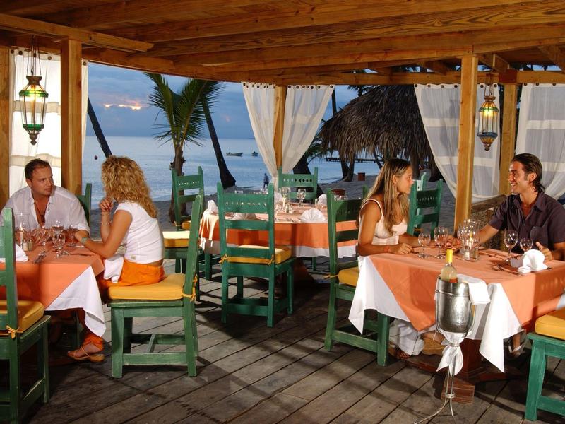Restaurant en plein air avec vue sur la mer, tables dressées avec des nappes orange et blanches.