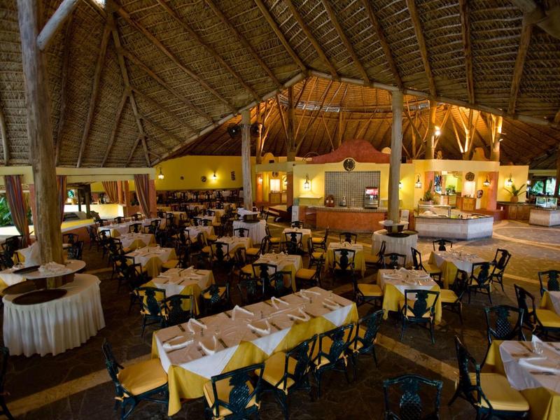 Grand restaurant ouvert avec tables dressées et plafond haut en chaume.