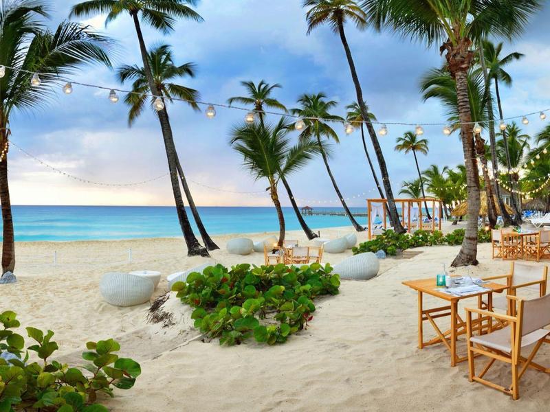 Plage avec palmiers, sable, tables et chaises à côté d'un restaurant au bord de la mer