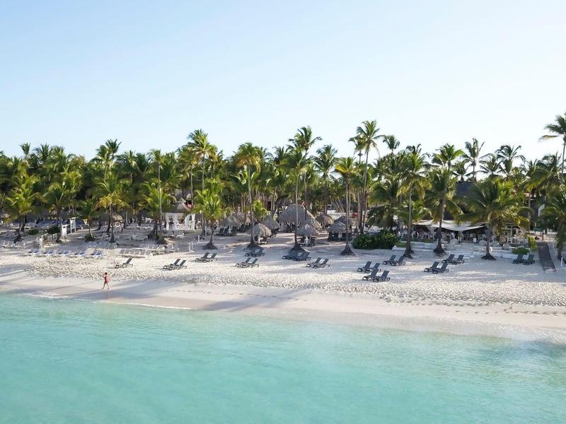 Longue plage de sable avec palmiers, parasols et chaises longues au bord de la mer turquoise.