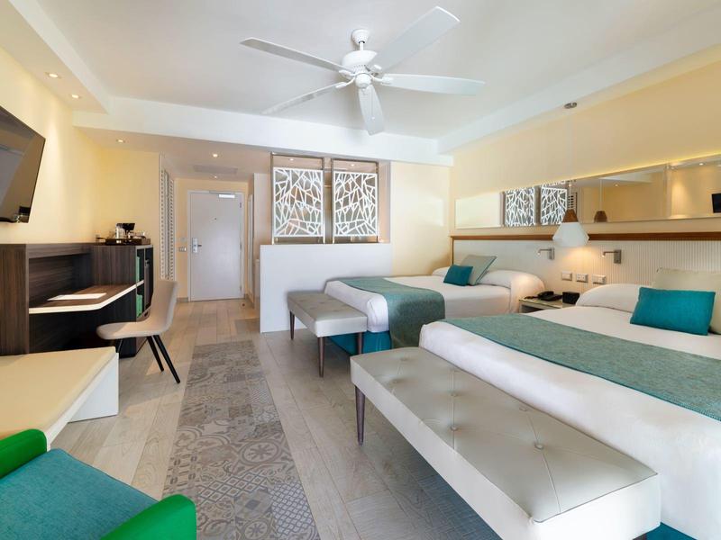 Chambre d'hôtel moderne avec deux lits, bureau, télévision et ventilateur de plafond.