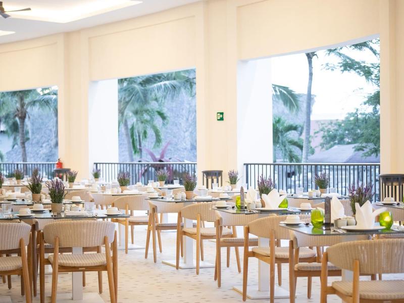 Restaurant élégant avec tables et chaises en bois et grandes fenêtres donnant sur des plantes vertes.