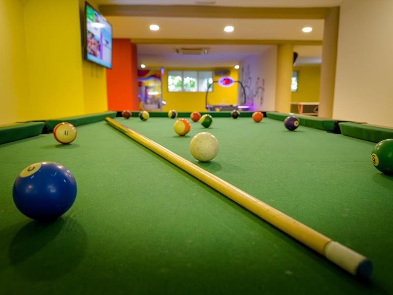 Grüner Billardtisch mit Queue und mehreren bunten Kugeln in einem gelb-orangen Raum.
