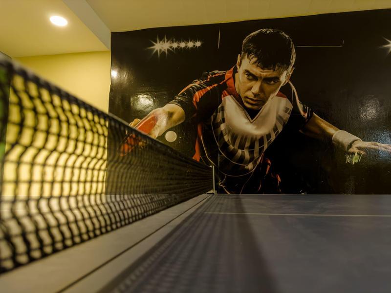 Tischtennisplatte mit Netz, im Hintergrund ein großes Wandbild eines Tischtennisspielers in Aktion.