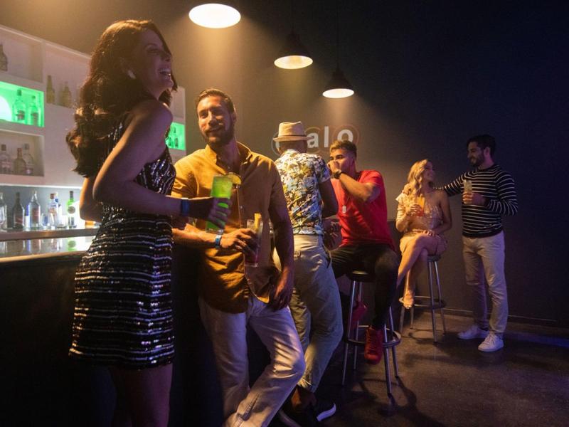 Sechs Personen in stilvoller Bar-Atmosphäre, gedämpftes Licht, Getränke, entspannte Stimmung.