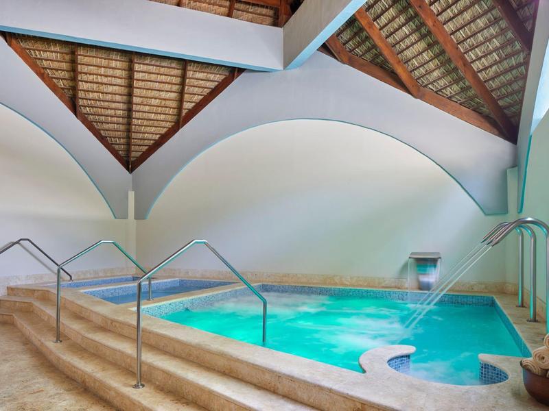 Innenraum mit einem rechteckigen Schwimmbecken, keramischem Boden und sichtbarer Holzbalkendecke.