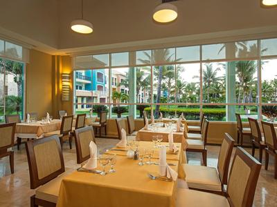 Restaurante luminoso con grandes ventanales con vista a palmeras y área exterior.