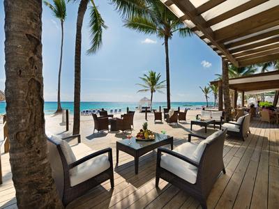 Open zitgedeelte met moderne stoelen en tafels op houten terras aan het strand bij zonnig weer.