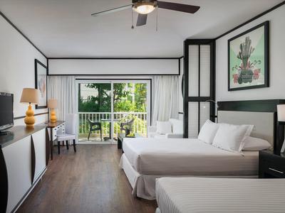 Habitación de hotel moderna con dos camas, TV y balcón con vistas a la vegetación.