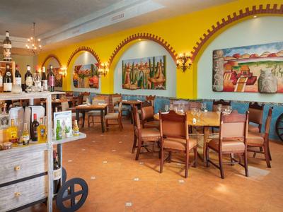 Un restaurante colorido con paredes amarillas, mesas y sillas de madera, y pinturas en las paredes.